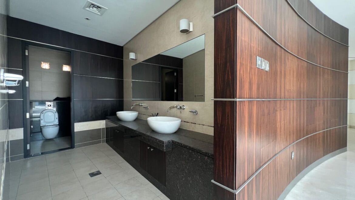 Front exterior of a modern, spacious four-bedroom independent villa in Al Heerah, Sharqan, Sharjah with a manicured lawn and driveway.-Propertyana real estate in dubai and sharjeh