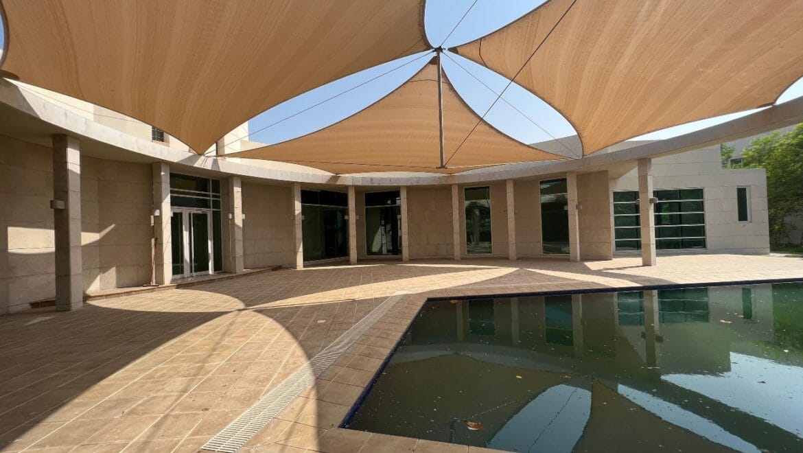 Front exterior of a modern, spacious four-bedroom independent villa in Al Heerah, Sharqan, Sharjah with a manicured lawn and driveway.-Propertyana real estate in dubai and sharjeh