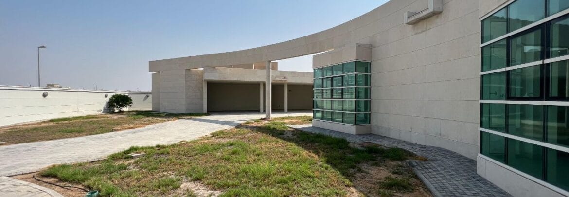 Front exterior of a modern, spacious four-bedroom independent villa in Al Heerah, Sharqan, Sharjah with a manicured lawn and driveway.-Propertyana real estate in dubai and sharjeh