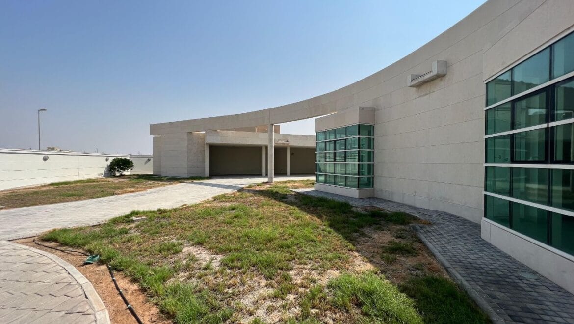 Front exterior of a modern, spacious four-bedroom independent villa in Al Heerah, Sharqan, Sharjah with a manicured lawn and driveway.-Propertyana real estate in dubai and sharjeh