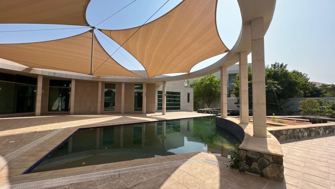 Front exterior of a modern, spacious four-bedroom independent villa in Al Heerah, Sharqan, Sharjah with a manicured lawn and driveway.-Propertyana real estate in dubai and sharjeh